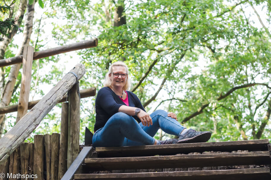 Cat Boersma sitting outdoors on wooden steps in the forest, smiling with openness and warmth, symbolizing guidance and support for expat women through nature therapy.