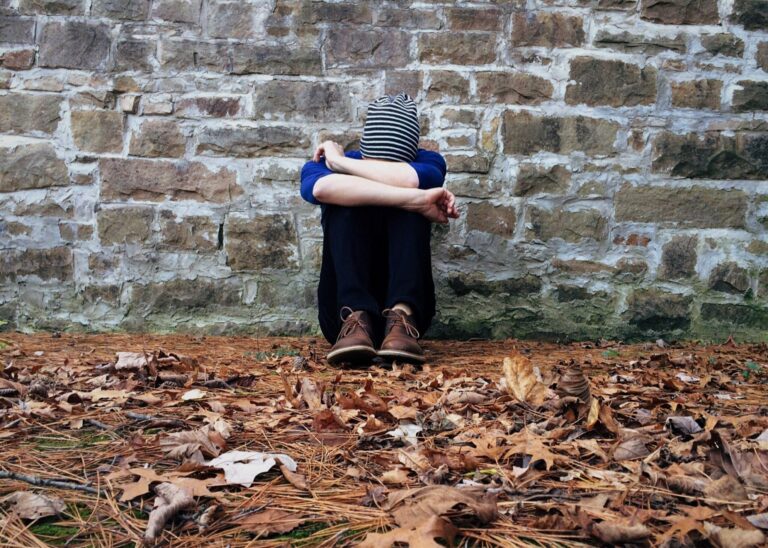 Woman sitting against a stone wall with her head down, feeling overwhelmed and isolated, symbolizing the loneliness many expat women experience.