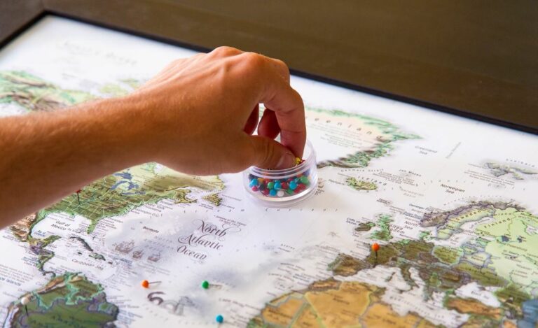 Hand placing colorful pins on a world map, symbolizing the journey, choices, and transitions of expat women seeking belonging and grounding.
