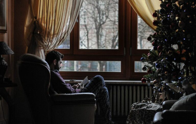Expat sitting alone at Christmas, reflecting by the window, highlighting holiday loneliness and the need for emotional support.
