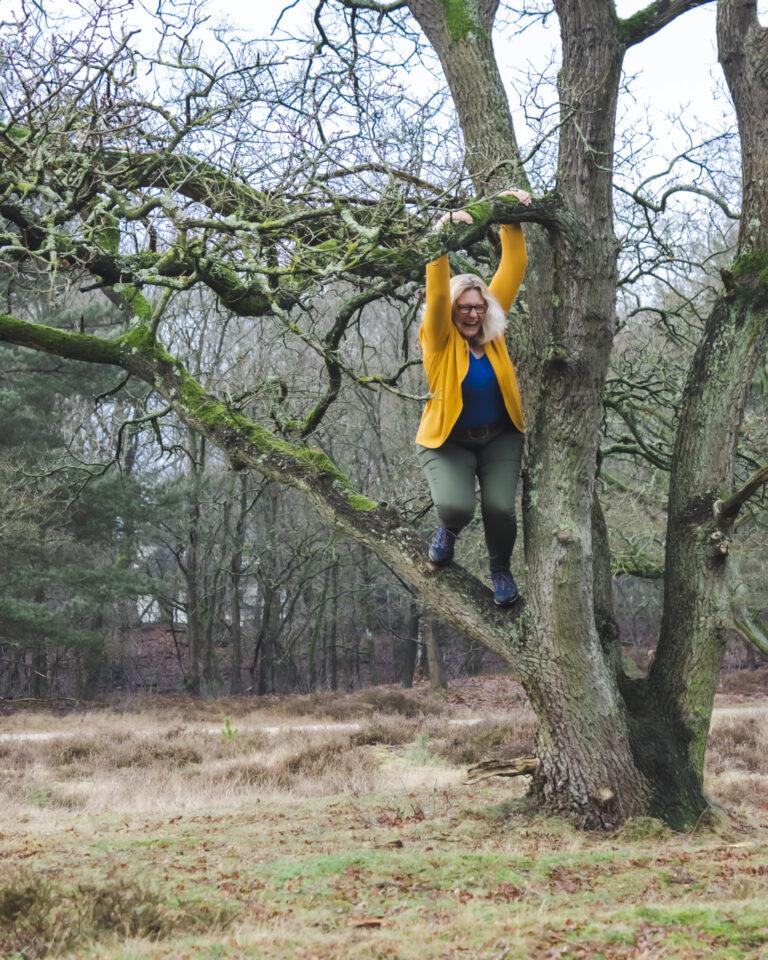 Woman smiling as she hangs from a tree branch, embodying courage, playfulness, and resilience for expat women navigating change.