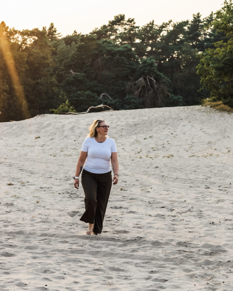 Cat Boersma walking barefoot on sand at sunrise, reconnecting with herself through nature therapy.